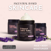 Ancestral Based Skincare Whipped Tallow Balm in a matte black jar with white cream on top, set against a soft pink background with lavender sprigs and two blurred jars behind it.