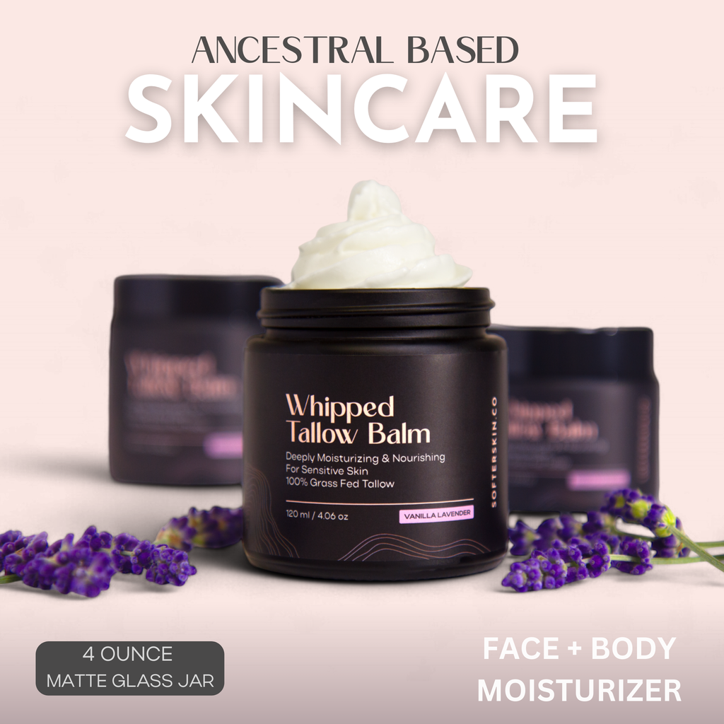 Ancestral Based Skincare Whipped Tallow Balm in a matte black jar with white cream on top, set against a soft pink background with lavender sprigs and two blurred jars behind it.