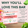 Nature's Aid handcrafted bar soap with greenery and text highlighting benefits on a pink background