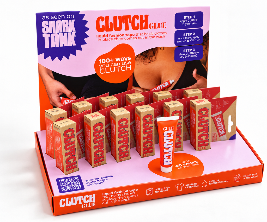 Clutch Glue liquid fashion tape retail display box with multiple small orange and brown tape rolls arranged in a pink and orange branded stand, plus a single tube of Clutch Glue in front.
