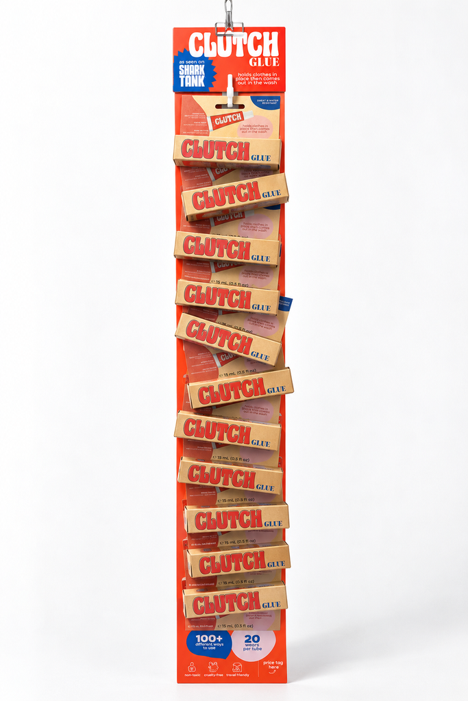 A retail display stand filled with multiple packs of Clutch Glee elastic bands, photographed against a clean white studio background. The display is orange and red with repeated product packaging visible.